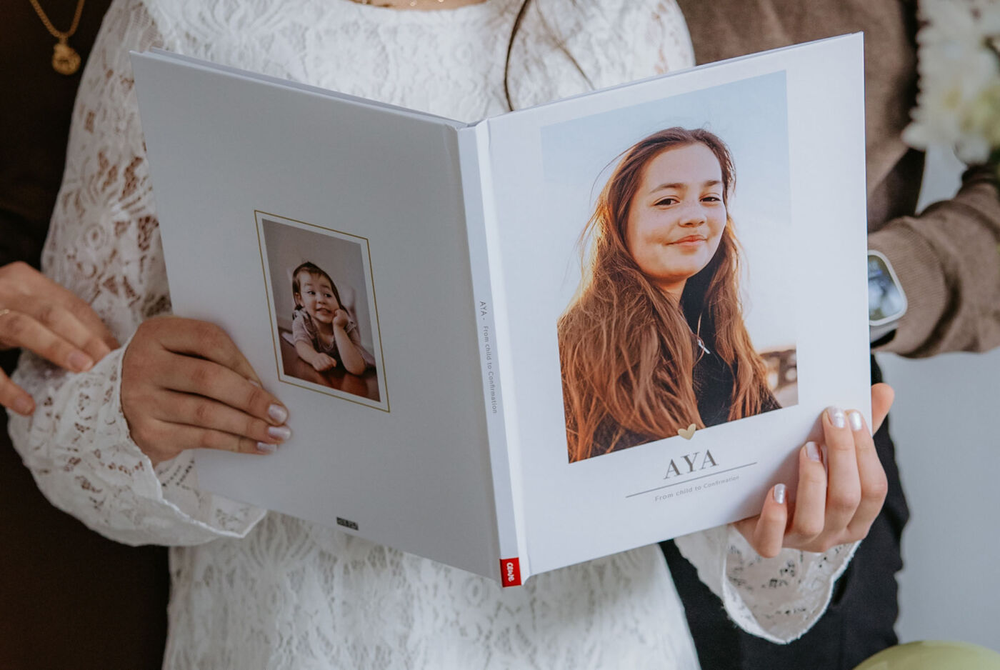 A person holds a CEWE photo book with a title on the cover.