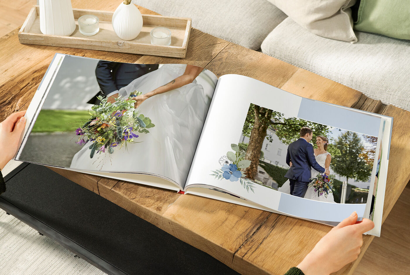 Two people flip through a CEWE photo book with wedding photos, surrounded by a warm wooden surface.
