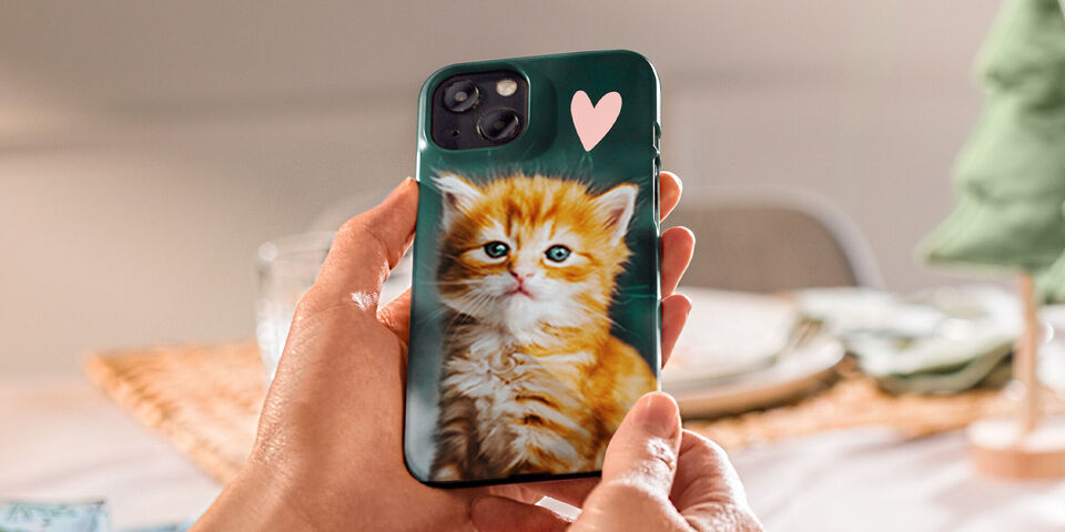 Little hands hold a phone with a cat design. The cover shows a cute orange kitten with blue eyes.