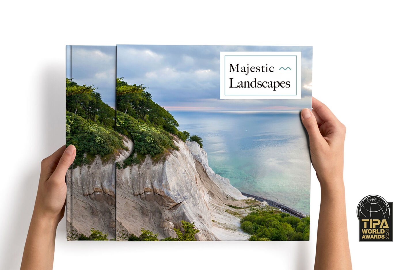 Two hands holding a photo book with a stunning landscape of a coastline.