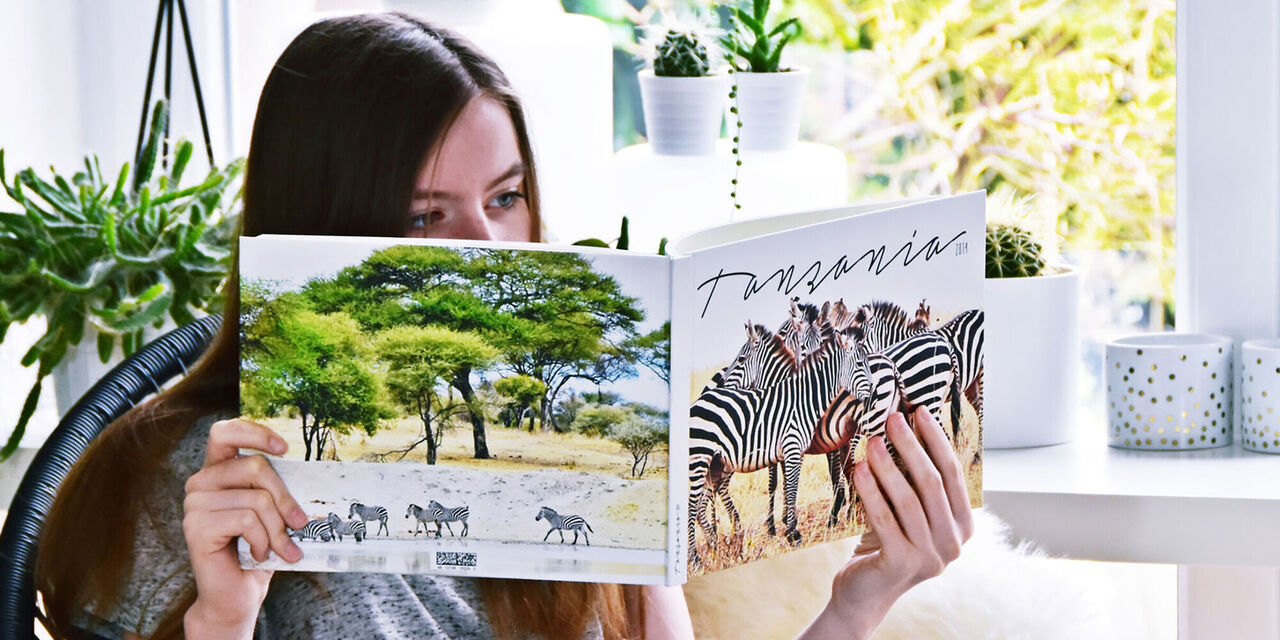 Nic's daughter is holding the African trip photo book open in her hands. There are photos of giraffes on both sides